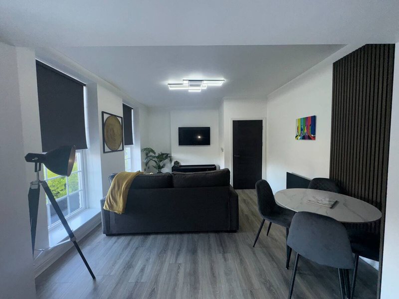 Modern living room with black sofa, dining table, wall-mounted TV and large window