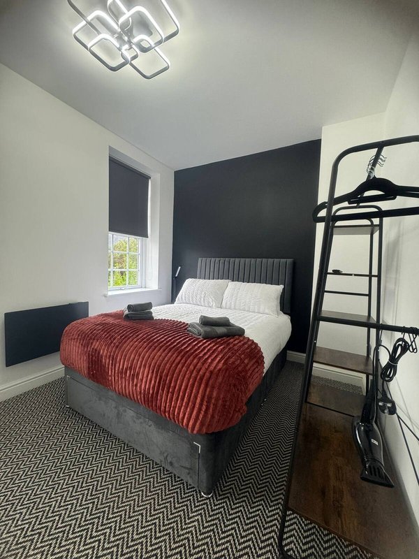 Bedroom with double bed, red blanket, dark feature wall, bunk bed, and window