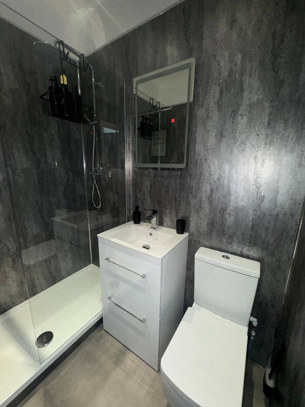 Modern bathroom with grey tile walls, white vanity unit, toilet, and walk-in shower enclosure