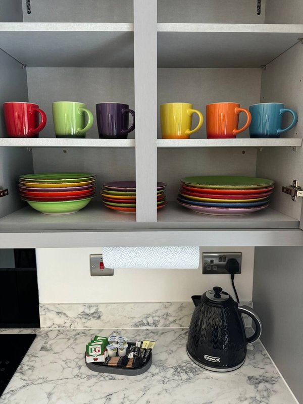 Open kitchen shelving with colorful ceramic mugs, bowls, electric kettle and countertop organizer