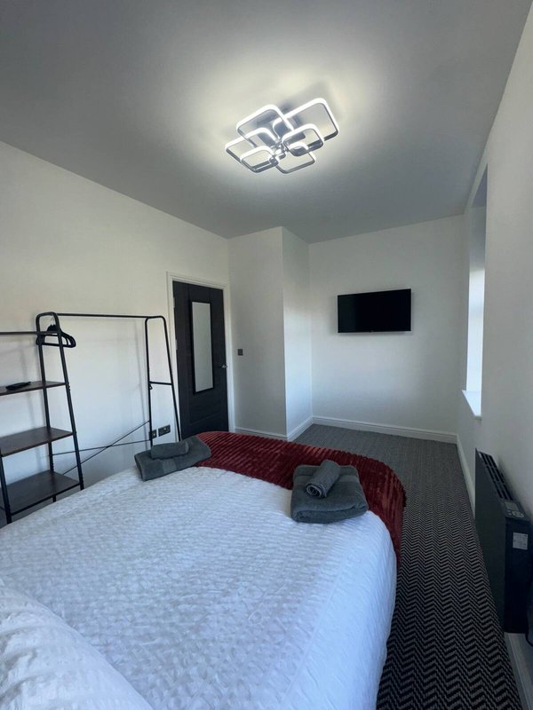 Bedroom with double bed, ceiling light fixture, wall-mounted TV and ladder shelf