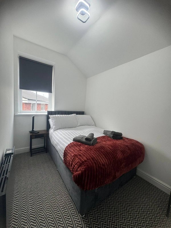 Small bedroom with single bed, red blanket, window with blind, and modern ceiling light