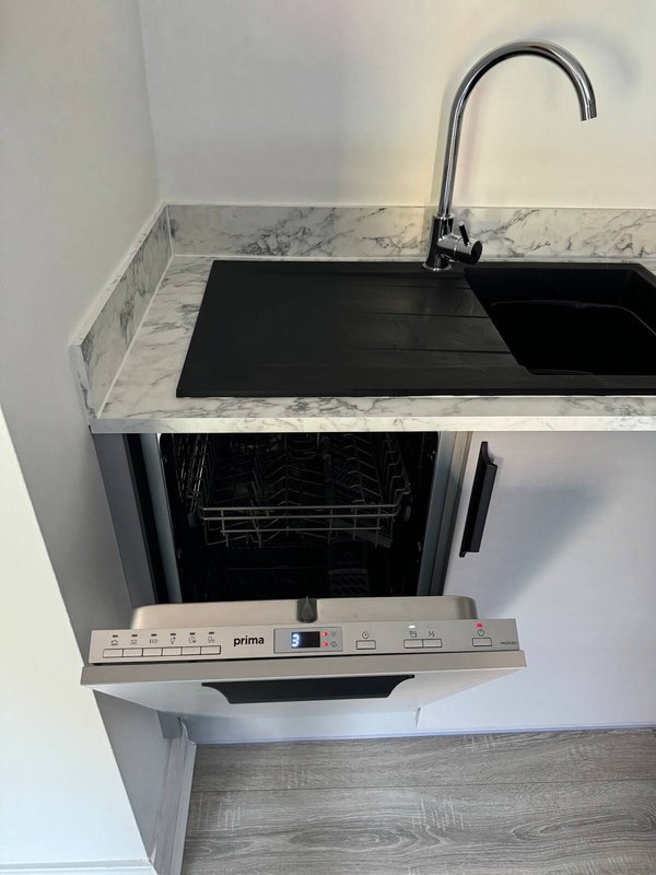 Compact kitchen corner with marble countertop, black sink, chrome faucet and integrated dishwasher