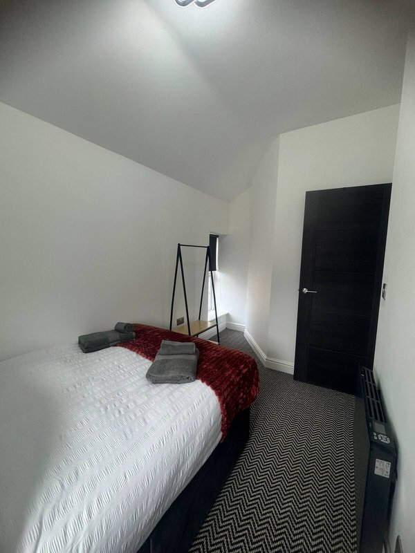 Bedroom with single bed, white bedding, red throw blanket, ladder shelf and dark door