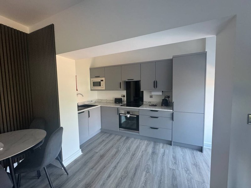 Modern open-plan kitchen with grey cabinetry, integrated appliances, and wooden-effect flooring