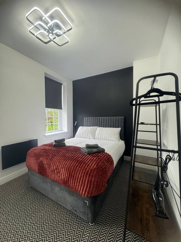 Modern bedroom with double bed, red blanket, black metal frame headboard, and neon ceiling light