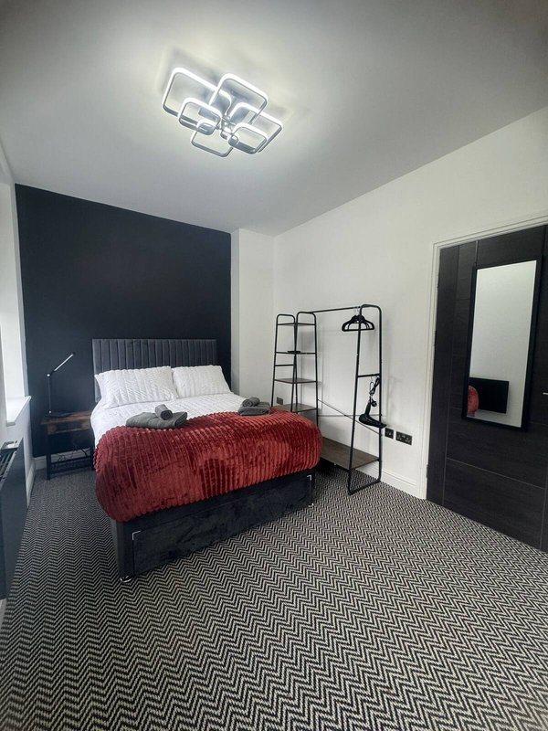 Modern bedroom with double bed, red bedding, dark accent wall, and geometric patterned carpet