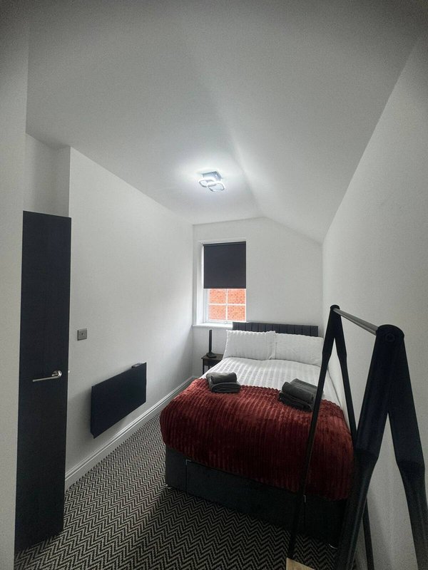 Compact bedroom with single bed, black metal frame, red bedding and white walls
