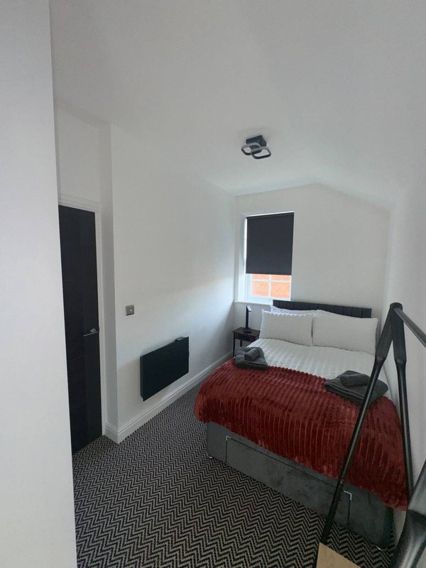 Compact bedroom with single bed, dark headboard, window with blind, and geometric floor pattern