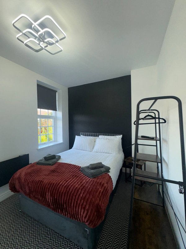 Bedroom with double bed, red bedspread, black accent wall, modern ceiling light and window