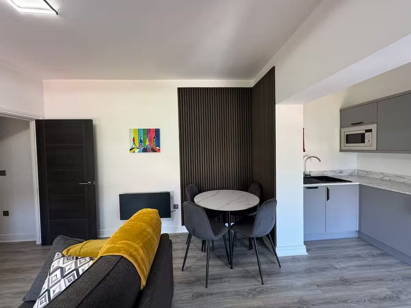 Open-plan living area with kitchen, dining table, sofa and colorful wall art