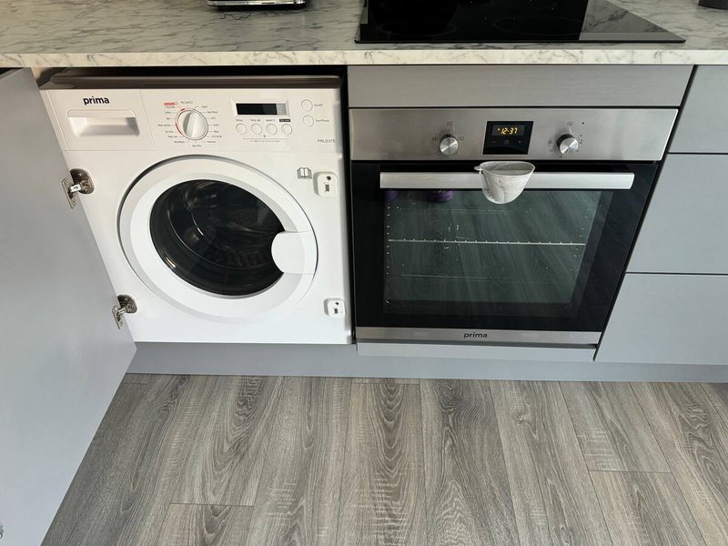 Integrated kitchen with white washing machine, black oven, and grey wood-effect flooring