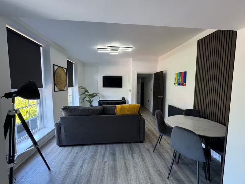 Open-plan living room with dark sofa, dining table, wall-mounted TV, and modern furnishings