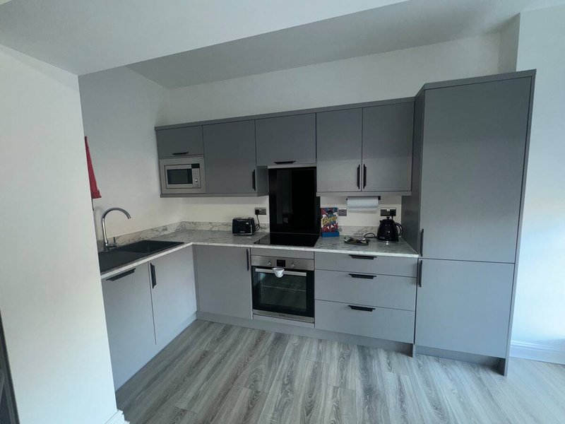 Modern kitchen with grey cabinetry, black appliances, white countertop and wooden flooring