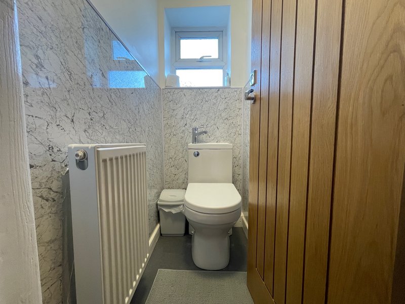 Small bathroom with toilet, radiator, marble-effect tiles, and wooden door