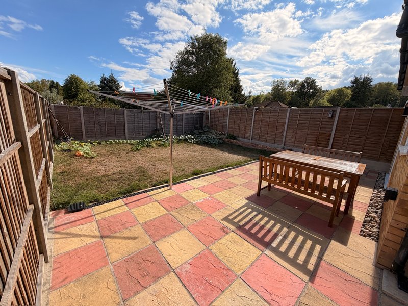 Patio garden with colored paving, wooden bench, fencing and grass area beyond
