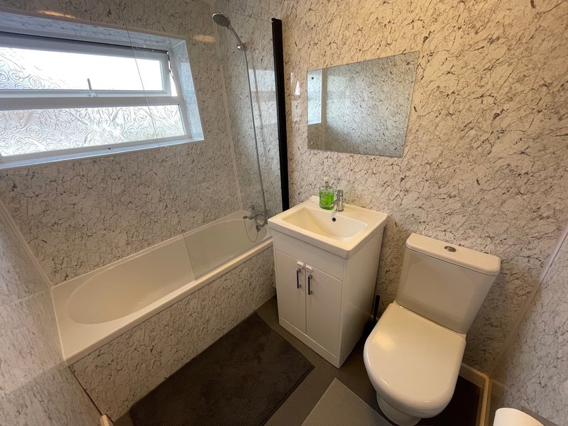 Modern bathroom with bathtub, pedestal sink, toilet, and cork-tile walls