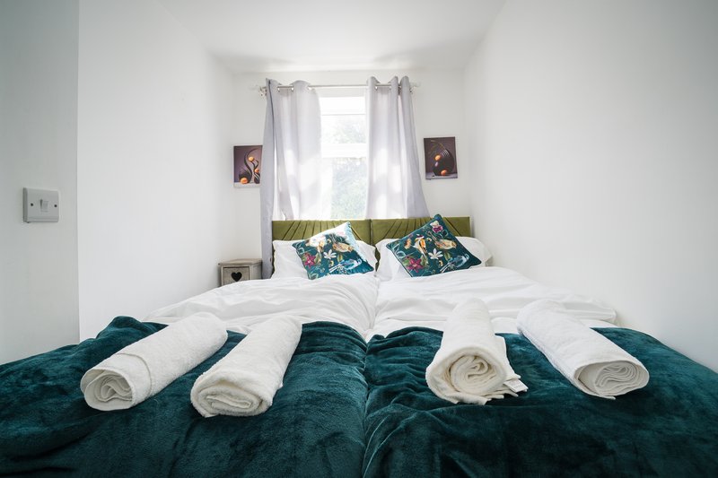 Bedroom with double bed, white rolled towels, teal bedding, window with curtains