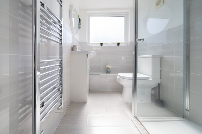 Modern bathroom with white tiles, walk-in shower, toilet, sink and heated towel rail