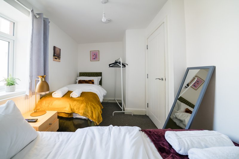 Bright bedroom with two beds, yellow bedding, wooden desk and window with curtains