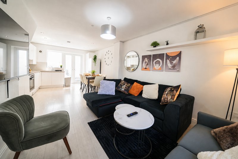 Open-plan living room with black sofa, green armchair, white coffee table and kitchen area