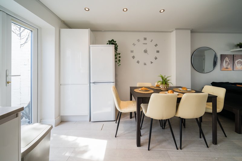 Modern open-plan kitchen and dining area with cream chairs, wooden table, and white appliances