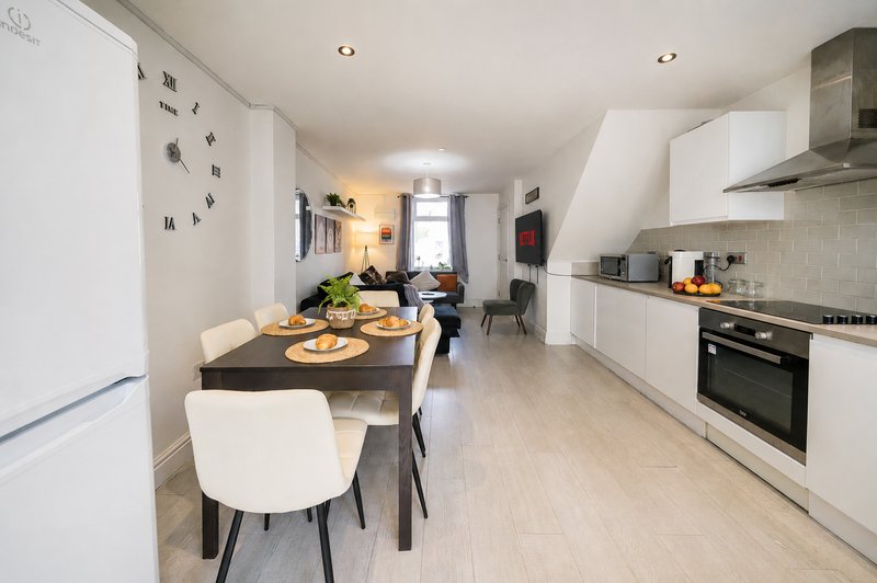 Modern open-plan kitchen and dining area with white cabinetry, black dining table, and staircase