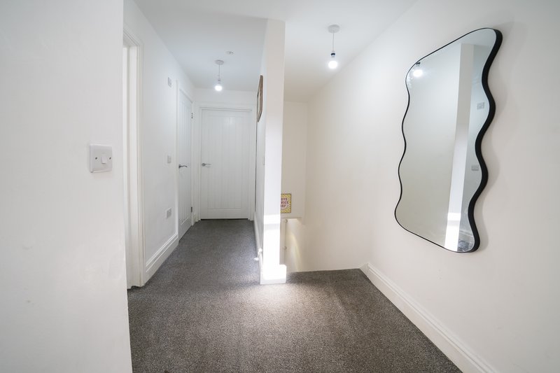 Bright modern hallway with gray carpet, white walls, wavy mirror, and doors leading to rooms