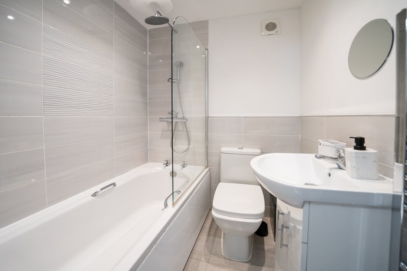 Modern bathroom with bathtub, glass shower screen, white sink and circular mirror
