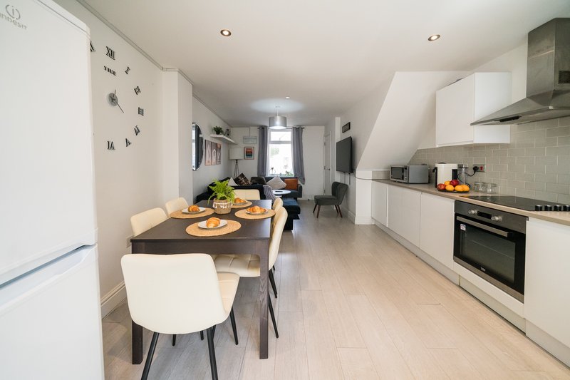 Modern kitchen-diner with white cabinetry, dining table, chairs, and wall clock