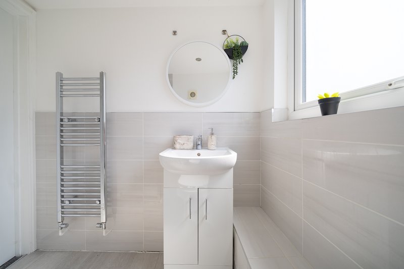 Clean modern bathroom with white pedestal sink, mirror, heated towel rail and potted plant