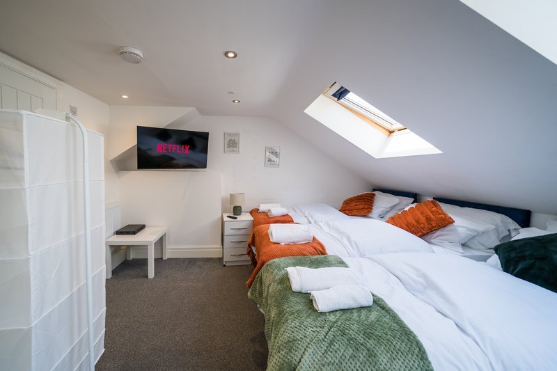 Attic bedroom with twin beds, orange and green bedding, wall-mounted TV, skylight and wardrobe.