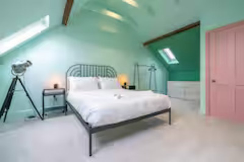 Bright attic bedroom with double bed, green accent wall, pink door and tripod lamp