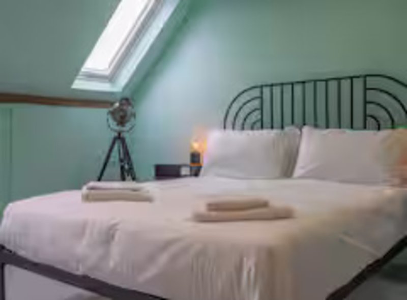 Bright attic bedroom with double bed, green walls, skylight and tripod lamp
