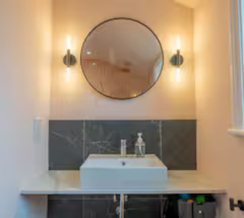 Modern bathroom with round mirror, wall sconces, white basin and dark backsplash
