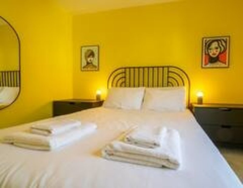 Bright yellow bedroom with double bed, black nightstands, wall art and bedside lamps