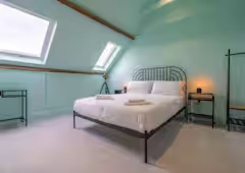 Bright attic bedroom with skylight, metal-frame bed, white bedding, and side tables