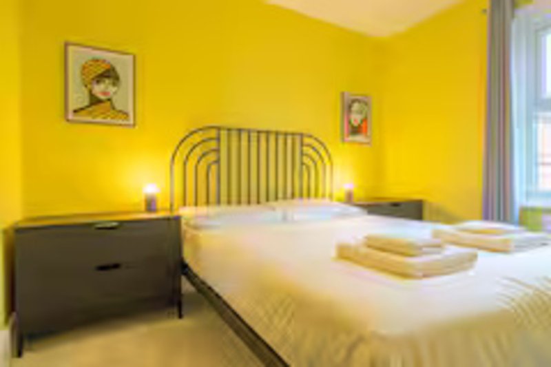 Bright yellow bedroom with double bed, black nightstand, bedside lamps and framed wall art
