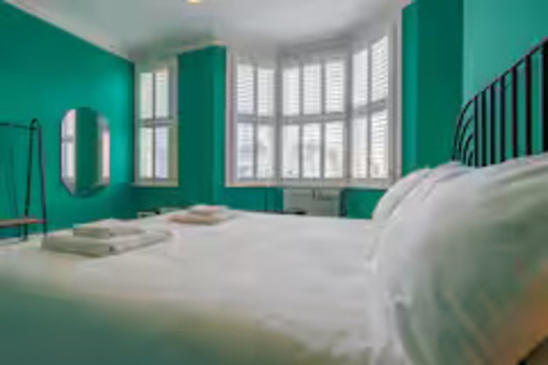 Bright bedroom with turquoise walls, white bedding, bay windows and metal headboard