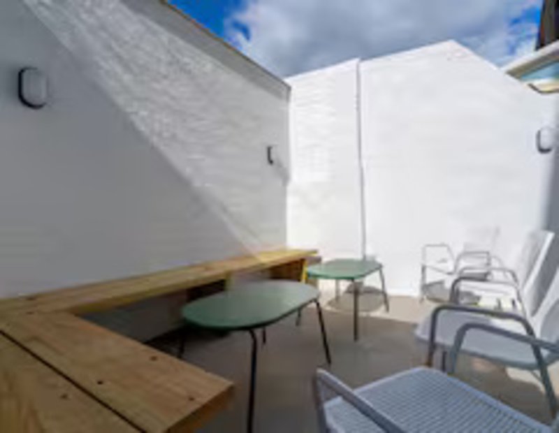 Modern outdoor patio with wooden bench, round table, and stacked chairs against white walls