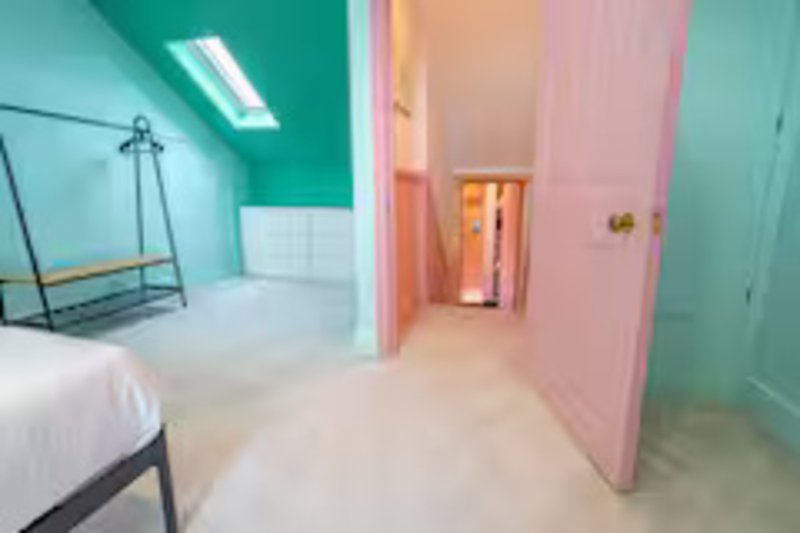 Modern bedroom with turquoise and pink walls, single bed, and doorway to ensuite bathroom