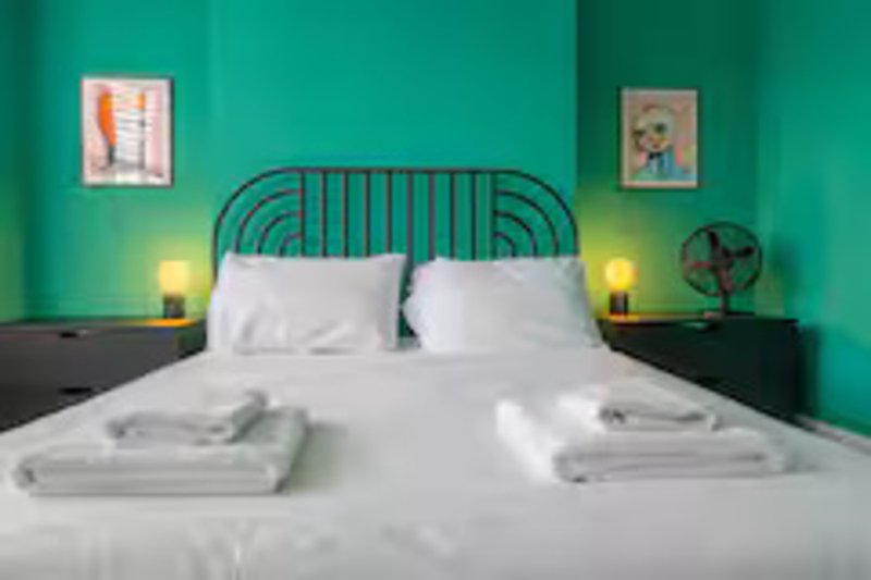 Bright bedroom with teal walls, metal bed frame, white bedding, and framed wall art