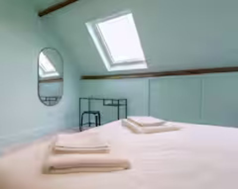 Bright attic bedroom with skylight, double bed, towels, and oval mirror