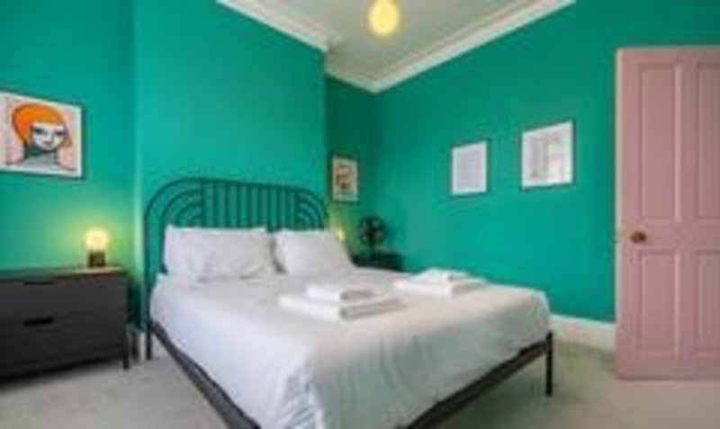 Bright turquoise bedroom with metal bed frame, white bedding, dark nightstand and pink door