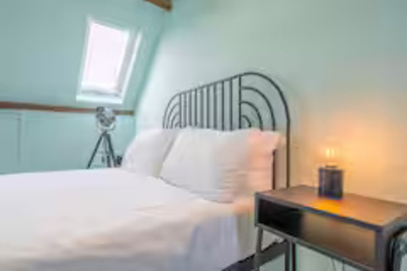 Bright attic bedroom with metal bed frame, white bedding, skylight window and bedside table