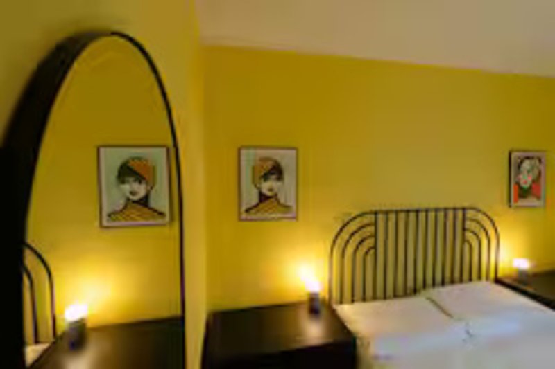 Bright yellow bedroom with arched floor lamp, bed with metal headboard, and framed wall art