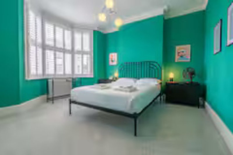 Bright turquoise bedroom with double bed, black frame, white bedding, and large window