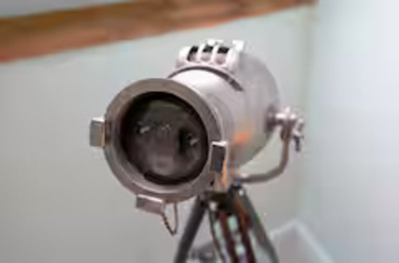 Vintage-style spotlight or theatrical lamp mounted on tripod against white wall