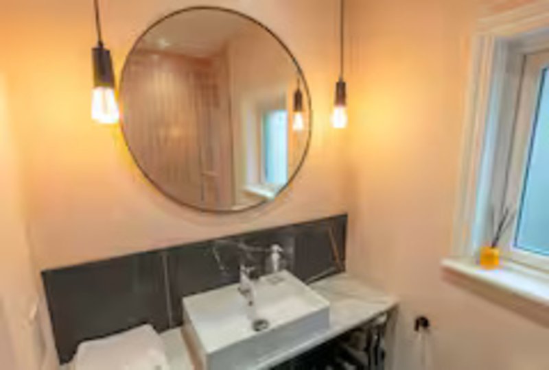Modern bathroom with round mirror, pendant lights, white sink and black vanity