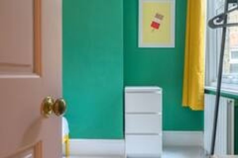 Colorful bedroom corner with green wall, white storage unit, brass doorknob and window